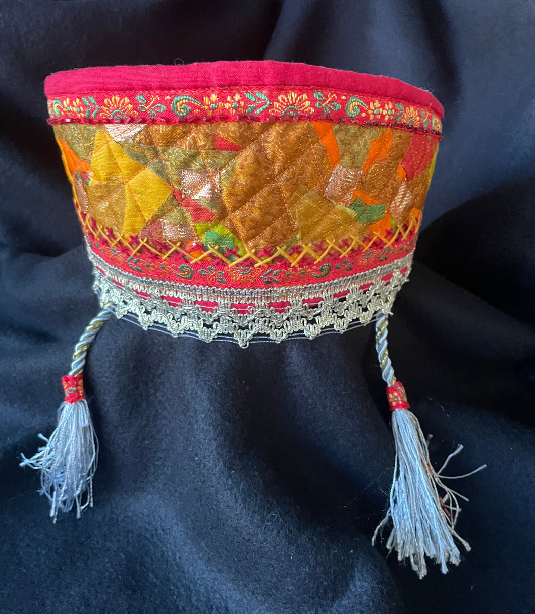 Decorative fabric head piece with intricate patterns and tassels on a dark background